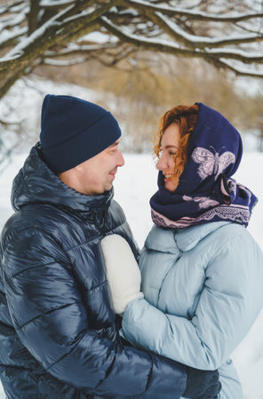 Love romantic love story. Happy couple of middle aged millennials, bright red-haired woman in winter snow park. Romantic date, kissing, hugging. Walking, having fun. Stylish blue clothes, jacket, hat.の写真素材