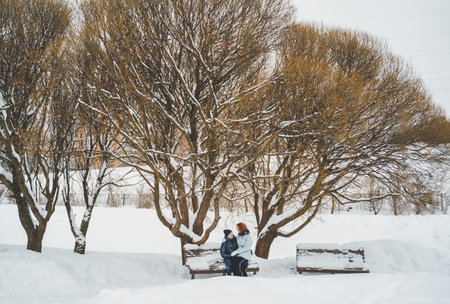 Love romantic love story. Happy couple of middle aged millennials, bright red-haired woman in winter snow park. Romantic date, kissing, hugging. Walking, having fun. Stylish blue clothes, jacket, hat.の写真素材