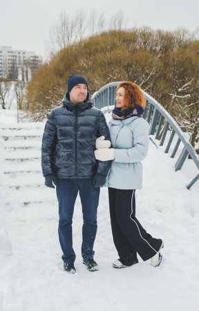 Love romantic love story. Happy couple of middle aged millennials, bright red-haired woman in winter snow park. Romantic date, kissing, hugging. Walking, having fun. Stylish blue clothes, jacket, hat.の写真素材