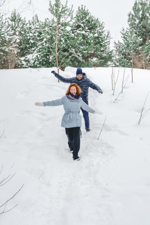 Love romantic love story. Happy couple of middle aged millennials, bright red-haired woman in winter snow park. Romantic date, kissing, hugging. Walking, having fun. Stylish blue clothes, jacket, hat.の写真素材