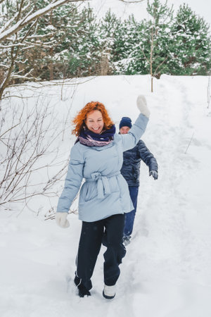 Love romantic love story. Happy couple of middle aged millennials, bright red-haired woman in winter snow park. Romantic date, kissing, hugging. Walking, having fun. Stylish blue clothes, jacket, hat.の写真素材