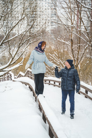 Love romantic love story. Happy couple of middle aged millennials, bright red-haired woman in winter snow park. Romantic date, kissing, hugging. Walking, having fun. Stylish blue clothes, jacket, hat.の写真素材