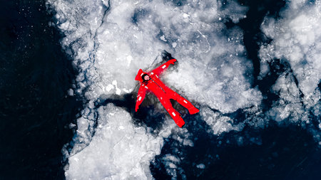 Aerial view of two people ice floating on icy water in bright red survival suits. Arctic frozen landscape. Extreme adventure, ice diving, cold water survival, winter expedition. Fun, outdoor activity.の写真素材