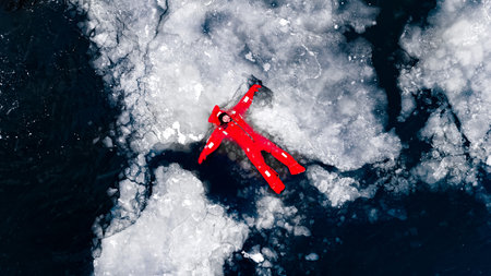 Aerial view of two people ice floating on icy water in bright red survival suits. Arctic frozen landscape. Extreme adventure, ice diving, cold water survival, winter expedition. Fun, outdoor activity.の写真素材