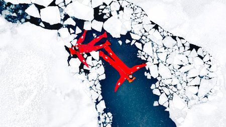 Aerial view of two people ice floating on icy water in bright red survival suits. Arctic frozen...