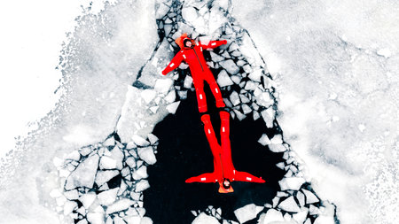 Aerial view of two people ice floating on icy water in bright red survival suits. Arctic frozen...