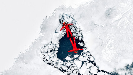 Aerial view of two people ice floating on icy water in bright red survival suits. Arctic frozen landscape. Extreme adventure, ice diving, cold water survival, winter expedition. Fun, outdoor activity.の写真素材