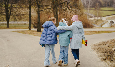 Teen girls walk together, hugging shoulders, each holding a skateboard. Jackets, jeans, sneakers show winter street style. Outdoor friendship, movement, balance, youth bonding, lifestyle and freedom.の写真素材