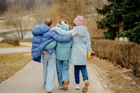 Teen girls walk together, hugging shoulders, each holding a skateboard. Jackets, jeans, sneakers show winter street style. Outdoor friendship, movement, balance, youth bonding, lifestyle and freedom.の写真素材