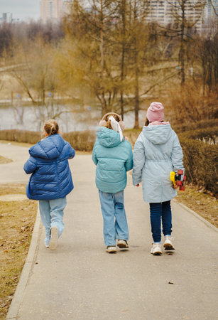 Teen girls ride skateboards on city path in winter park. Jackets and jeans reflect urban youth style. Street sport improves balance, movement, coordination, friendship and outdoor fun for kids.の写真素材