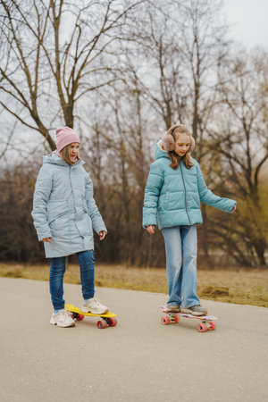 Girls ride colorful skateboards in city park. Autumn trees, jackets, jeans and sneakers show seasonal style. Youth enjoy outdoor activity, balance, skating, motion, sport, childhood fun and freedom.の写真素材