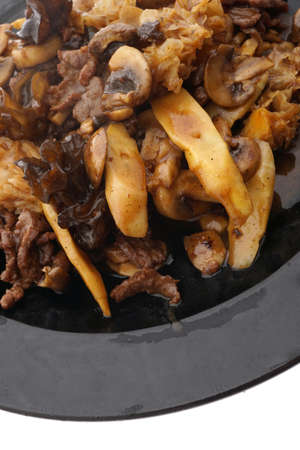 Chinese food. Veal with black and white mushrooms and bamboo shoots in black plate isolated on white. Closeup.の写真素材