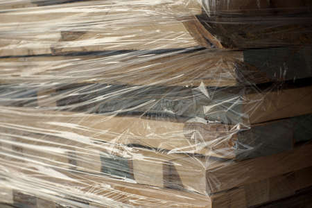 Wooden planks stacked in rows wrapped in plastic foil. Close up