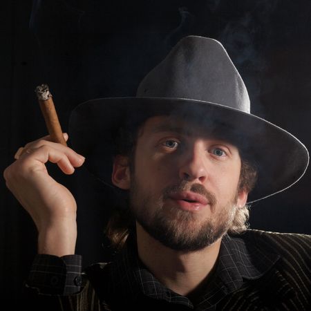 A handsome man in a grey hat smoking a cigar