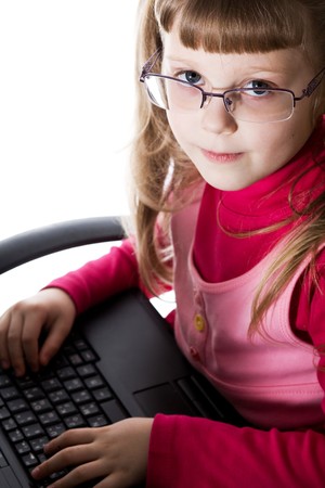An image of a cute little girl in glasses with laptop on her kneesの写真素材