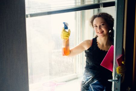 An image of a woman in yellow gloves washing the window