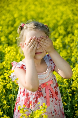 Little girl playing hide and seek in yellow fieldの写真素材