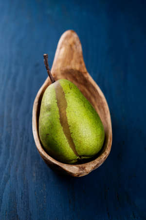 Ripe pear in a wooden bowl on a blue backgroundの写真素材