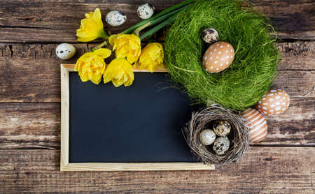 Easter decorations and black board with copy space on wooden background.の写真素材