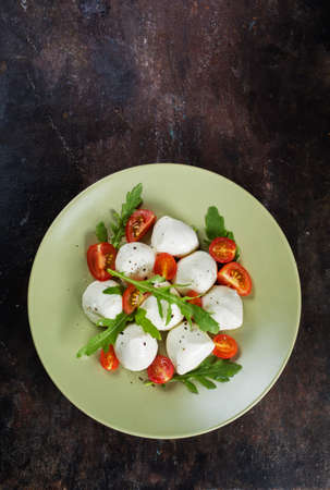 Mozzarella, cherry tomatoes and arugula on a rustic dark  backgroundの写真素材