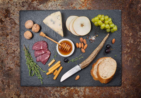 Mixed Antipasto: cheese and grapes, honey,nuts, pears on a rustic dark backgroundの写真素材