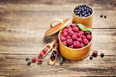 Raspberries and blueberries in a bowl on rustic wooden background. Food background, copyspaceの写真素材