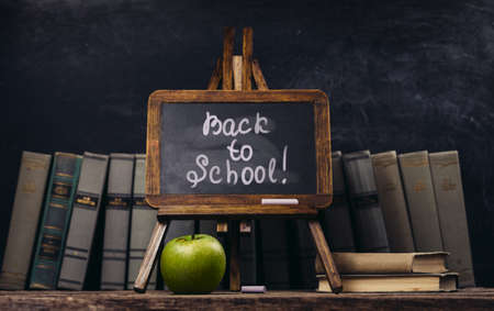 Back to school concept. Background with vintage blackboard, alarm clock, old books, green appleの写真素材