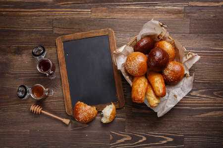 Fresh baked buns with jam and blank black board on a wooden table. Free space for text.の写真素材