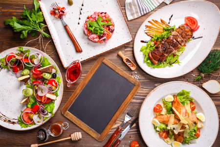 Different salads and Black Chalk Board, top view. Vegetable salad, Salad with smoked duck, Grilled chicken Caesar salad. Copy space.の写真素材