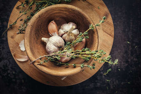 Garlic and thyme in a wooden bowl on a dark table from above.の写真素材
