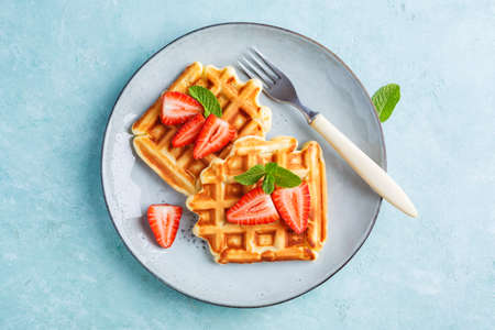 Homemade belgian waffles with strawberrieson a blue background. Tasty breakfast with waffles.の写真素材