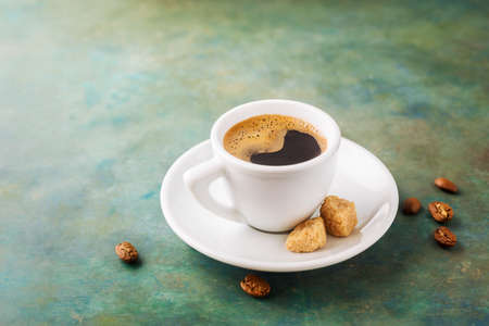 Hot coffee in white cup on a green background and sugar. Copy space.の写真素材