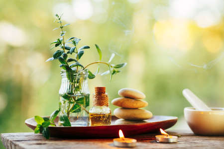 Beautiful composition with natural mint essential oil, zen stones and burning candles outdoorsの写真素材