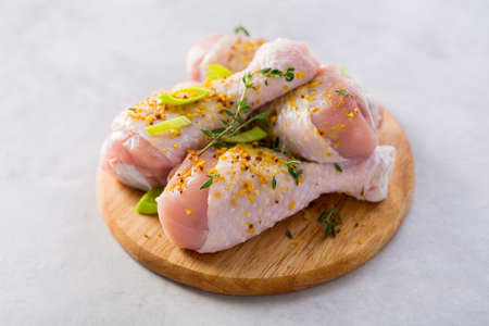 Raw chicken legs with spices in small wooden board on a light grey textured backgroundの写真素材