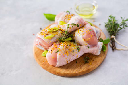 Raw chicken legs in small wooden board on a light grey textured backgroundの写真素材