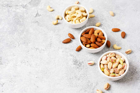 Assortment of nuts, cashew, pistachio almond in a bowls on a light background with copy space.の写真素材