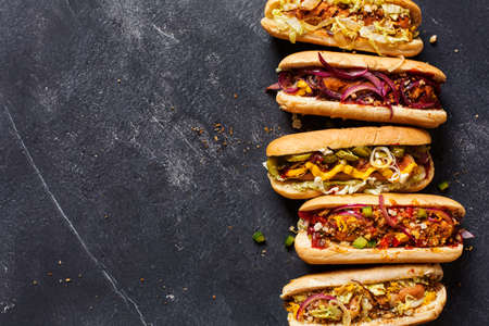 Hot dogs with different toppings on a dark background. Food background with copy space, top view. Fast food.の写真素材