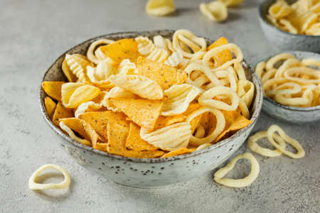 Crispy potato chips and onion rings and nachos in bowlの写真素材