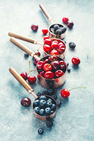 Different berries in copper measuring cups, blackberries, cherries and blueberriesの写真素材