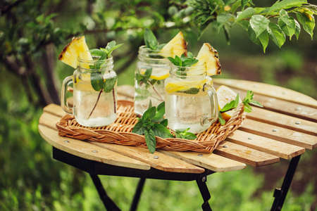 Cooling drink with lemon and mint decorated with a slice of pineapple on the garden table.の写真素材
