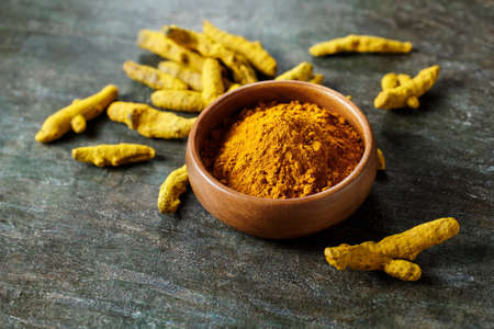 Turmeric powder in a bowl and turmeric root.の写真素材