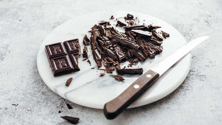 Cut into pieces of dark chocolate on a marble board, close-up. Ingredients for baking.の写真素材