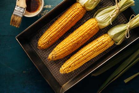 Fresh corn cobs on a baking tray with oil and spices. Natural products, healthy food.の写真素材