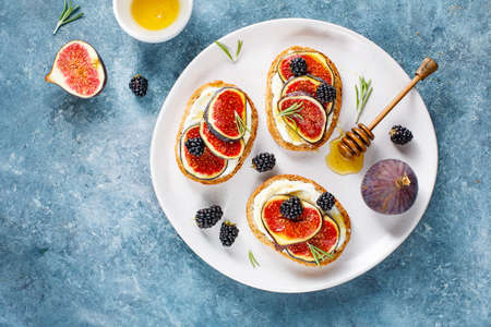 Sandwiches with fresh figs, blackberries and honey on a white plate. Free space for text. Top view.の写真素材