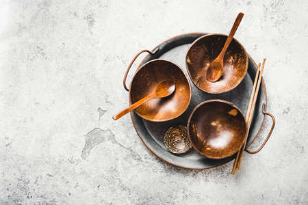 Three empty coconut bowls with spoon on a tray. Top view, copy space.の写真素材