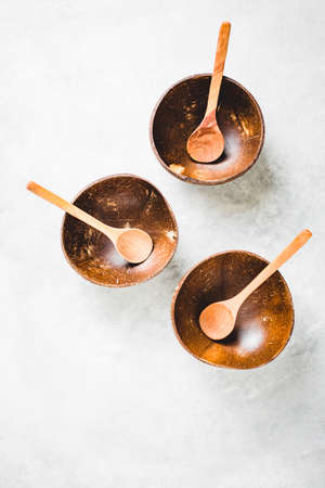 Three empty coconut bowls with spoon on gray background. Top view.