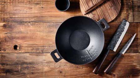 Set of dishes for Asian cuisine, small cast iron wok, Japanese knives on a wooden background.の写真素材