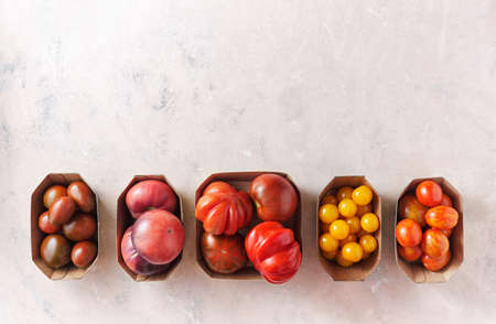 Different types of tomatoes in paper packaging on a shabby pink background, top view.の写真素材