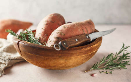 Sweet potatoes in a large wooden bowl with rosemary, close up.の写真素材