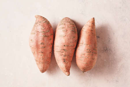 Three large sweet potatoes on a textured pink background, top view.の写真素材